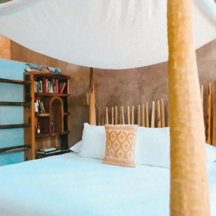 A rustic villa bedroom with wooden bookshelves, a canopy bed, and a decorative orange pillow.