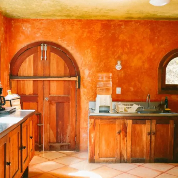 A rustic villa kitchen with orange-red walls, wooden doors, and tiled floors.