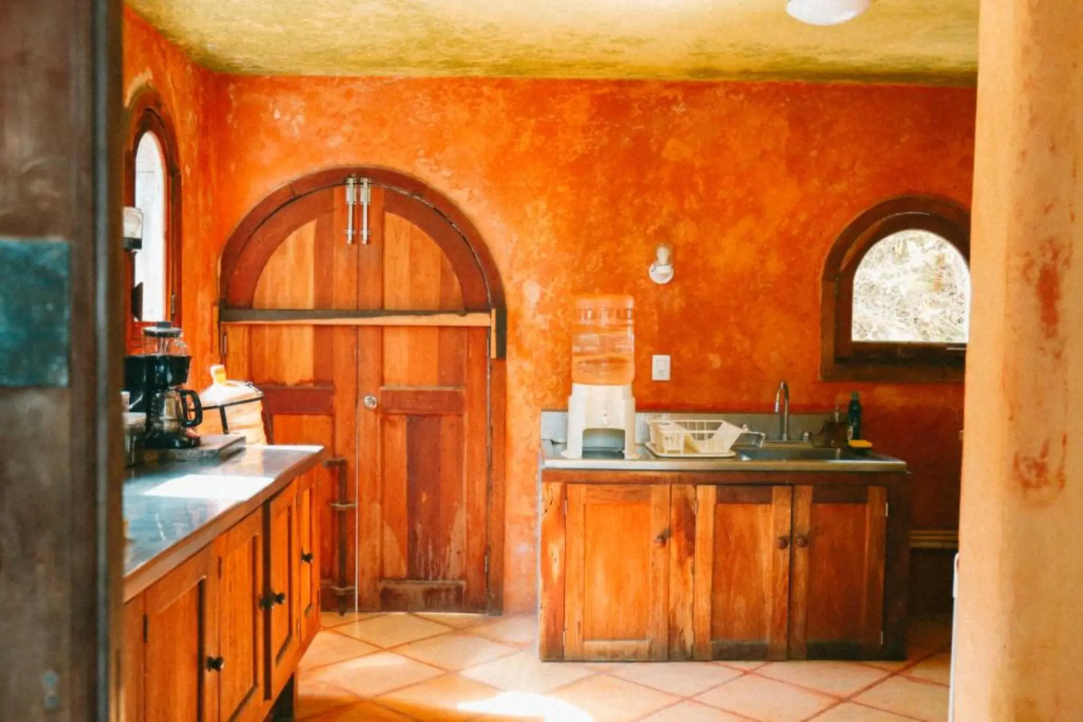 A rustic villa kitchen with orange-red walls, wooden doors, and tiled floors.