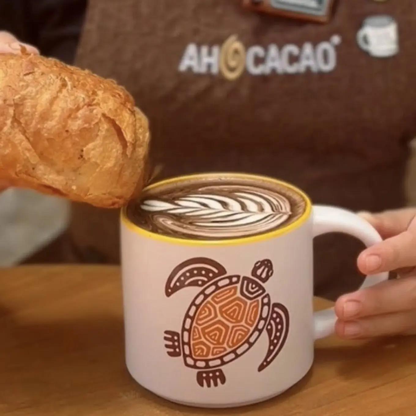 person dipping puff pastry in a mug of hot chocolate at ah cacao cafe