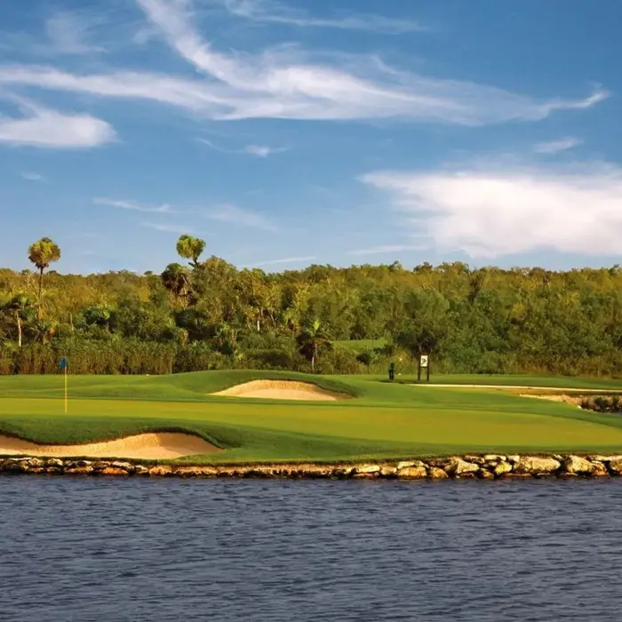 A beautifully manicured island golf green surrounded by a stone retaining wall, tranquil water, and dense tropical jungle at Moon Palace Golf Course.