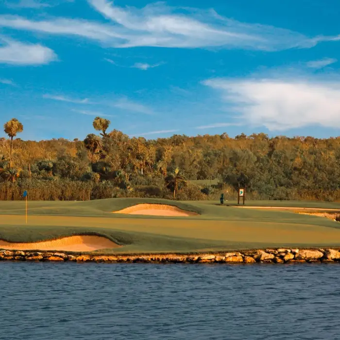 A pristine island golf green surrounded by a tranquil water hazard and natural rock formations against a backdrop of lush tropical jungle