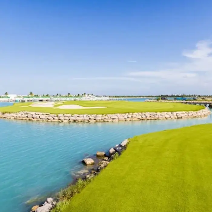 Luxury yachts docked in the pristine marina with the championship golf course fairways visible just across the bright blue water