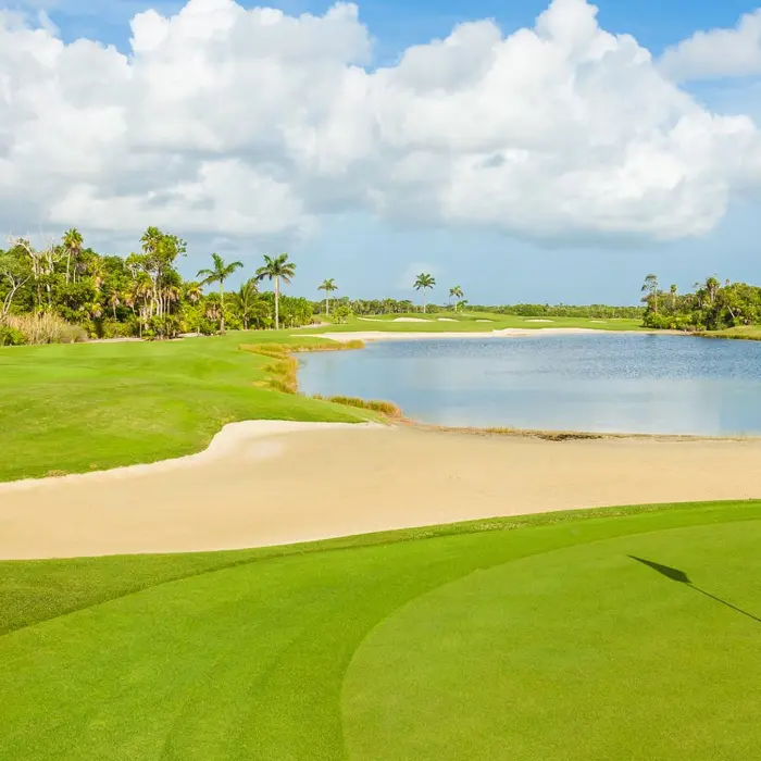 A pristine golf green and white flag bordering a large sand bunker and a peaceful lake at the luxury Moon Palace Golf Course in Cancún.